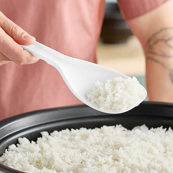 A person holding an Avantco rice paddle spoon over a bowl of rice.