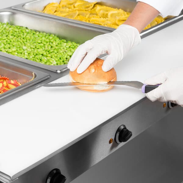 A person in gloves using an Avantco cutting board to slice a bun.