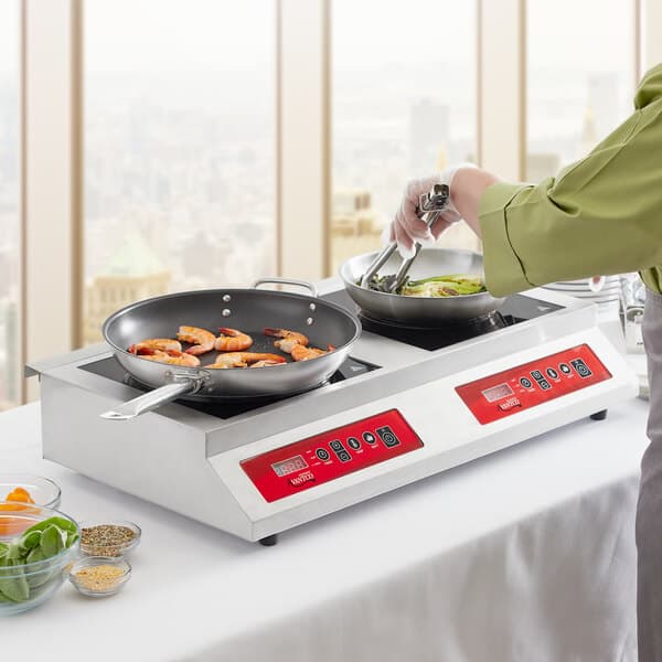 A woman using an Avantco double countertop induction range to cook shrimp in a pan.