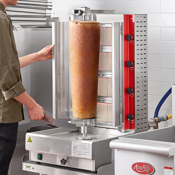 A man using an Avantco gas vertical broiler to cook a large piece of meat.