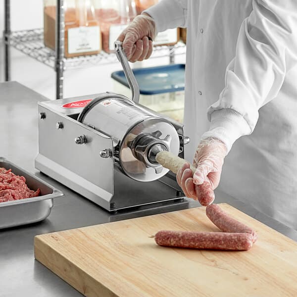 A person in a white coat and gloves using an Avantco horizontal manual sausage stuffer to make sausages.