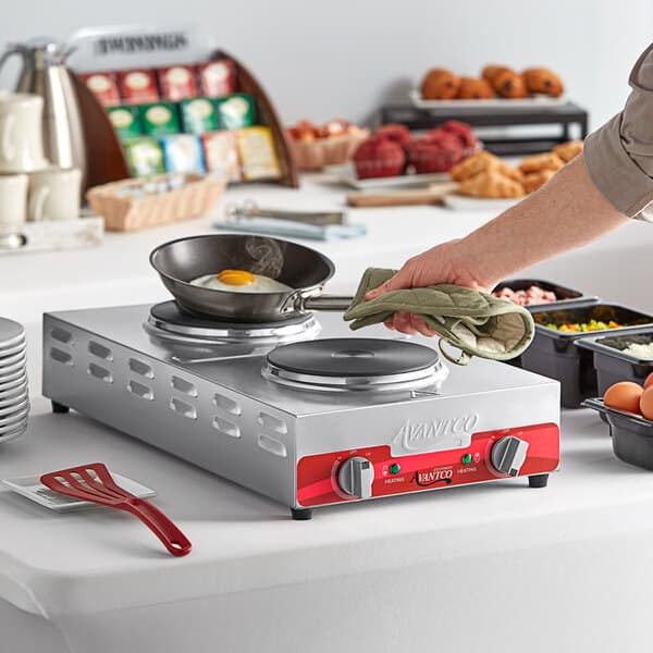 A person cooking a fried egg on an Avantco portable electric stove.