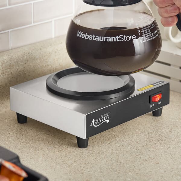 A hand pouring coffee into an Avantco decanter on a counter.