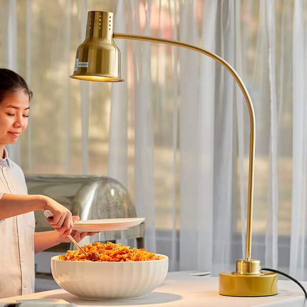 A woman using an Avantco gold flexible heat lamp to serve pasta from a white bowl.