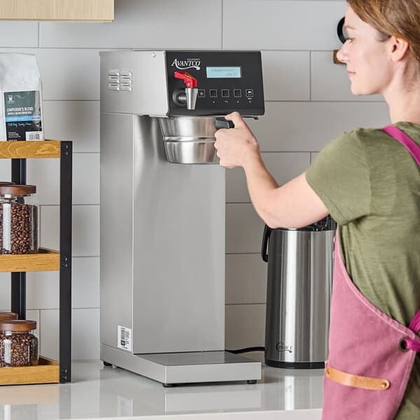 An Avantco CMADAP digital automatic airpot coffee maker on a countertop with a person operating it.