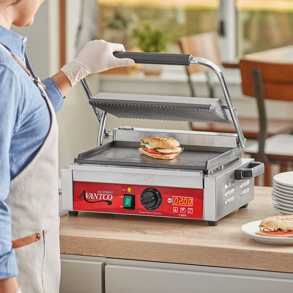 A person cooking a sandwich on an Avantco commercial panini grill.