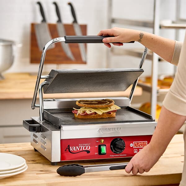A woman using an Avantco commercial panini grill to cook a sandwich.