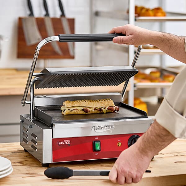 A person using an Avantco commercial panini grill to cook a sandwich.
