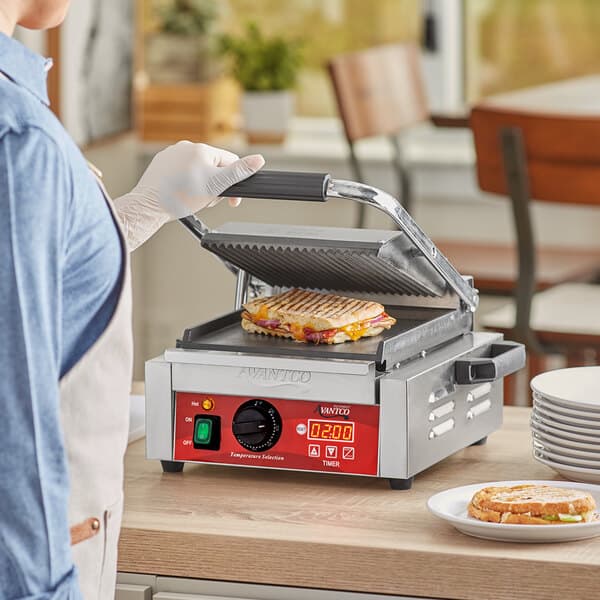 A person using an Avantco commercial panini grill to cook a sandwich.