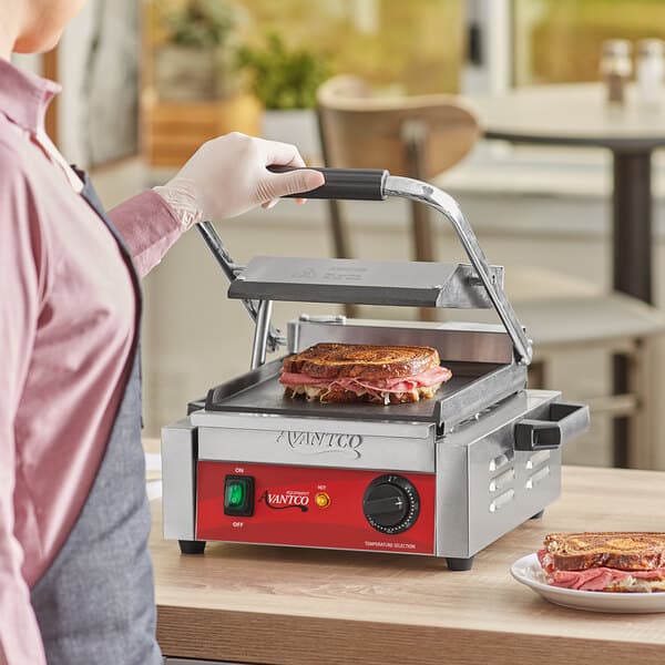 A person using an Avantco commercial panini grill to cook a sandwich.