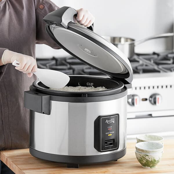 A woman using an Avantco non-stick pot to cook rice in a rice cooker.