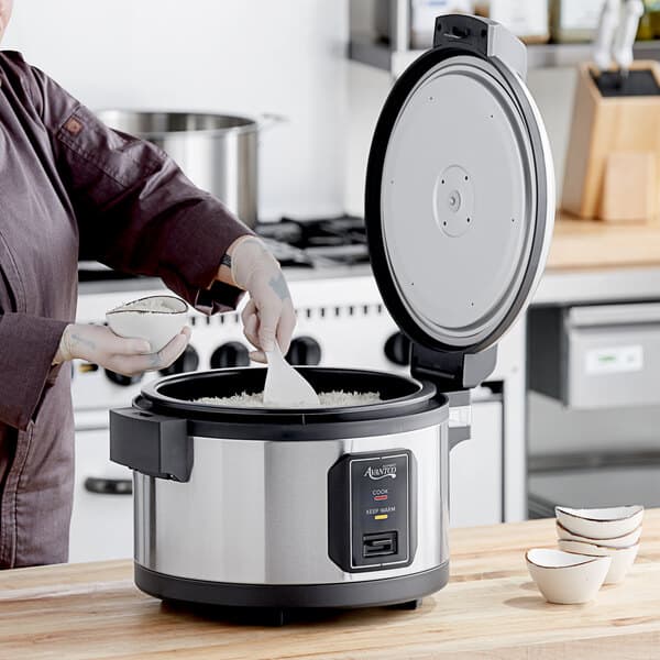 A woman using an Avantco non-stick pot to cook rice in a large electric cooker.