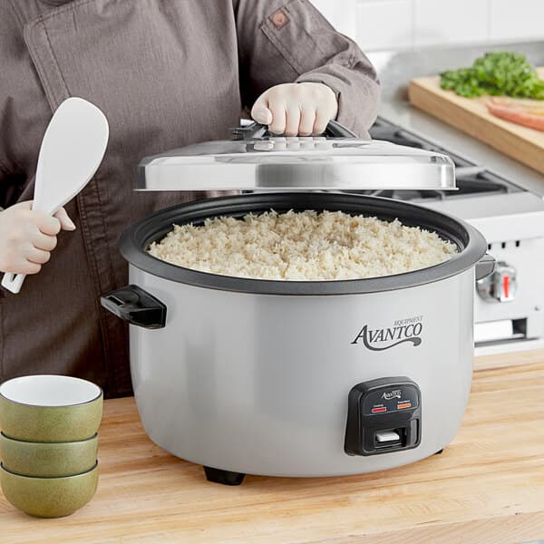 A person using an Avantco stainless steel lid to cook rice in a rice cooker.