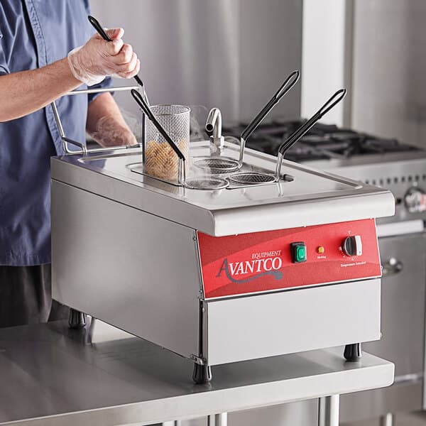 A man using an Avantco electric countertop pasta cooker to cook food.