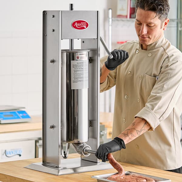 A man in a chef's coat using an Avantco stainless steel vertical manual sausage stuffer.